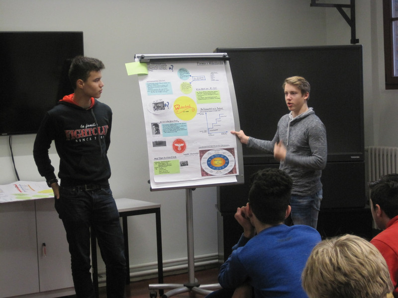 Auf dem Foto rechts erläutern Schülerinnen und Schüler an einer Moderationswand die Ergebnisse ihrer Projektarbeit.